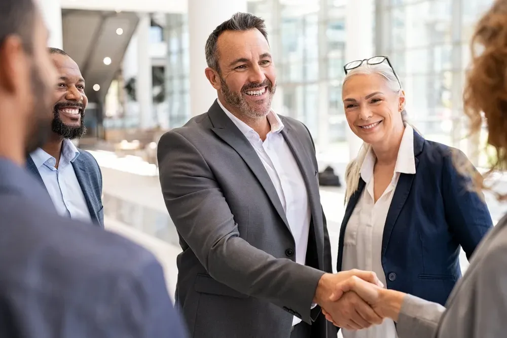 Happy mature businessman shaking hands with businesswoman in modern office. Successful entrepreneur greeting business woman with